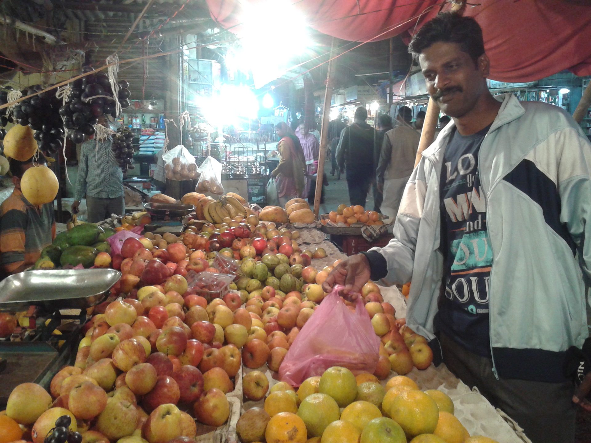 A fruit seller weighing pomegranates at a market stall in Vadodara